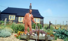 Derek Jarman stands in the driftwood garden at the front of Prospect Cottage