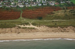 This photograph shows the 1945 WWII V2 crater once some 100 metres back from the dune edge. It was employed as a delightful sandy sun-trap, snugly out of the wind. Now the sea is about to break through the remains of the last dune to flood the entirety of the Great Winterton Valley. The floor of this valley is the original beach, which accreted to become enclosed by a series of high dunes until three years after intense offshore aggregate dredging commenced. Since then it has reversed by demonstrating continuous and escalating erosion.  